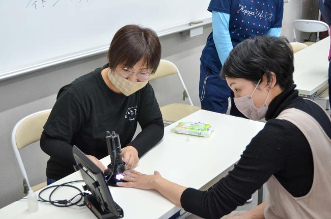 毛細血管観察スコープで血流などを観察する参加者と講師の斎藤さん